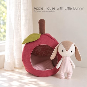 May include: A red apple-shaped fabric house with a brown stem and a green leaf, featuring an open front with a pink patterned interior. Beside it stands a small stuffed bunny with a tan face, long ears, and a pink and white striped body. Text reads: Apple House with Little Bunny Beginner to intermediate.