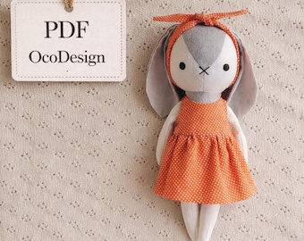 May include: A handmade plush bunny doll with gray ears and a white and gray face. The doll wears an orange polka-dot dress and matching headband. A tag with the text "PDF OcoDesign" hangs nearby.