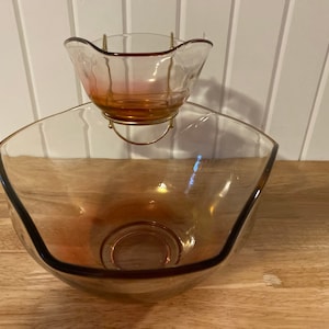 May include: A two-tiered glass serving dish with a clear bowl and a smaller, amber-coloured bowl on top. The bowls are connected by a metal stand.