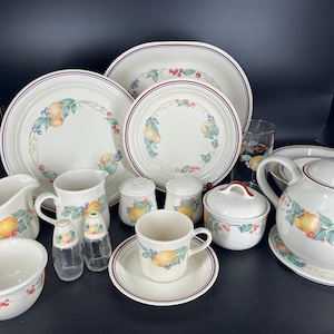 Puede incluir: Un juego de vajilla de cerámica blanca con un patrón floral que presenta limones, hojas y bayas. El juego incluye platos, tazones, una jarra de crema, un azucarero, una tetera y saleros y pimenteros.