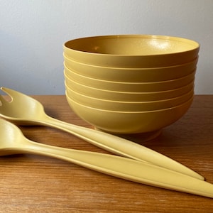Könnte beinhalten: Ein Satz von sechs gelben Plastikschalen, die übereinander gestapelt sind. Zwei gelbe Salatbesteck aus Plastik liegen auf einer Holzoberfläche.