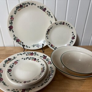 Peut inclure: Un ensemble de vaisselle crème avec un motif de nichoir et de vigne. L'ensemble comprend des assiettes, des assiettes à salade et des bols. Les assiettes ont une bordure décorative avec des nichoirs et des accents violets.