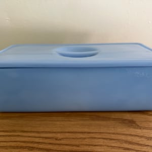 Peut inclure: Une boîte à mouchoirs rectangulaire bleu clair avec un dessus arrondi et une petite indentation au centre du couvercle.
