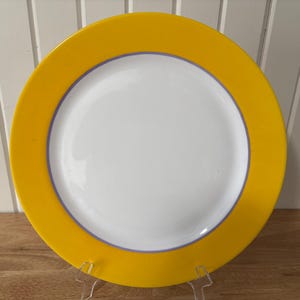 May include: A white ceramic mug with a black handle and the text "But First, Coffee" in a bold, black font. The mug is set against a blurred background, suggesting a cozy setting.