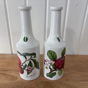 May include: A white ceramic mug with a black handle and the text "But First, Coffee" in a bold, black font. The mug is set against a blurred background, suggesting a cosy setting.