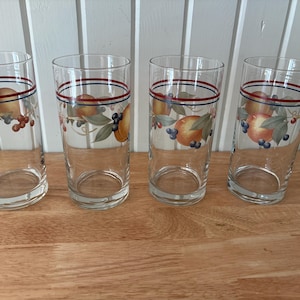 Peut inclure: Quatre verres à boire transparents avec un motif de fruits. Chaque verre a une rayure rouge et bleue près du bord et un motif de pêches, de raisins et de feuilles. Les verres sont sur une surface en bois.
