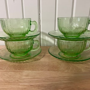 Può includere: Quattro tazze da tè e piattini in vetro verde vintage con un motivo a grappolo d'uva. Le tazze e i piattini sono impilati a coppie.