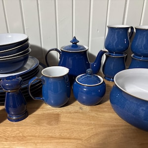 Pode incluir: Um conjunto completo de louça de cerâmica azul e branca. O conjunto inclui tigelas, pratos, canecas, uma chaleira, um açucareiro e saleiros e pimenteiros. A louça tem um acabamento brilhante e um interior branco.
