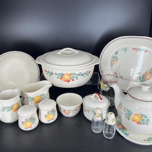 Puede incluir: Un juego de vajilla de cocina de cerámica blanca con un patrón floral que presenta limones amarillos, bayas rojas y hojas verdes. El juego incluye una cacerola con tapa, una tetera, un tazón para servir, una jarra de crema, un azucarero, dos saleros y pimenteros y un tazón pequeño.