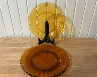 May include: Two amber glass plates with a scalloped edge. The plates are stacked on top of each other. The top plate is slightly larger than the bottom plate.