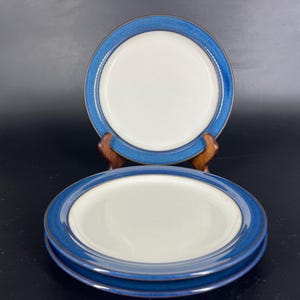 May include: Three blue and white ceramic dinner plates stacked on top of each other. The plates have a blue rim and a white centre.
