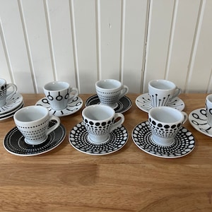 Pode incluir: Conjunto de oito xícaras de espresso brancas e pires com padrões geométricos pretos. As xícaras e os pires têm uma variedade de designs, incluindo círculos, linhas e pontos.
