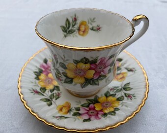 Può includere: Un set da tè bianco con bordo dorato e motivo floreale. I fiori sono gialli, rosa e verdi.