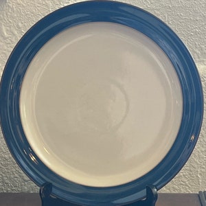 Peut inclure: Une assiette plate blanche avec un bord bleu foncé. L'assiette a un bord légèrement surélevé.