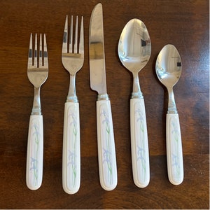 Può includere: Set di cinque posate argentate con manici bianchi con un motivo floreale. Il set comprende un coltello da burro, una forchetta da tavola, un cucchiaio da tavola e due cucchiaini.