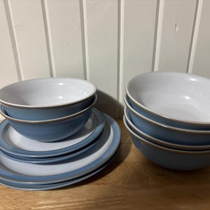 Può includere: Un set di ciotole e piatti in ceramica blu e bianca. Le ciotole hanno una forma arrotondata con interno bianco ed esterno blu. I piatti presentano anche un design blu e bianco. Il set è disposto su una superficie di legno.
