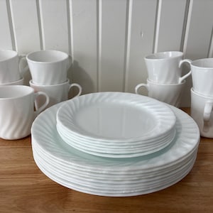 May include: A collection of white ceramic plates and mugs. The plates feature a spiral pattern around the rims. The mugs have a matching spiral design and a handle. The set includes plates and mugs.
