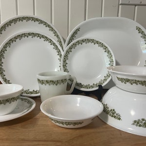 Op de afbeelding: Een set witte keramische schalen met een groen bloemenpatroon. De set bevat een grote ovale schaal, twee dinerborden, twee saladeschalen, een mok, een kleine kom en een grote kom.