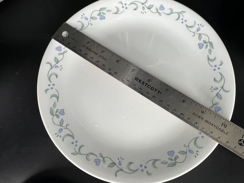 Może przedstawiać: Biały ceramiczny talerz obiadowy z zielonym i niebieskim wzorem kwiatowym wok&oacute;ł krawędzi. Talerz ma średnicę 23 cm.