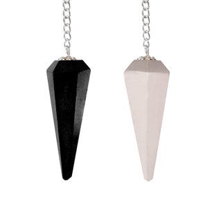 May include: Two pendulums, one black and one white, hang from silver chains. Each pendulum has a faceted, cone-like shape. The background is plain white, highlighting the contrast between the two pendulums. The pendulums are likely used for divination or spiritual practices.