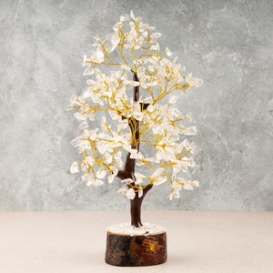 May include: A crystal tree with clear quartz crystals and gold wire branches. The tree is on a wooden base and has a snowy white base.