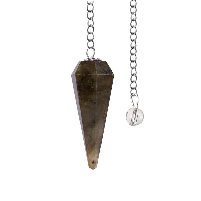 May include: A faceted, elongated pendulum made of a dark, speckled stone, suspended by a silver-colored chain. A small, clear crystal bead hangs from a separate chain. The pendulum is designed for divination and spiritual practices.