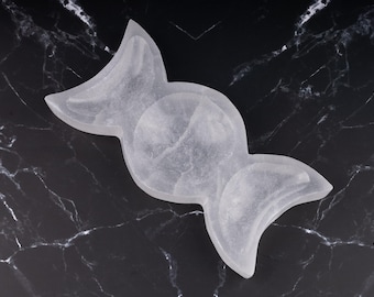 Puede incluir: Plato de selenita blanco en forma de media luna. El plato está tallado en forma de tres medias lunas y es perfecto para guardar objetos pequeños como joyas o cristales.