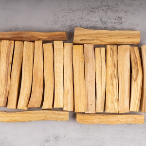May include: A collection of natural Palo Santo sticks, arranged in a rectangular shape on a gray background. The sticks are light brown in color and have a slightly curved shape.