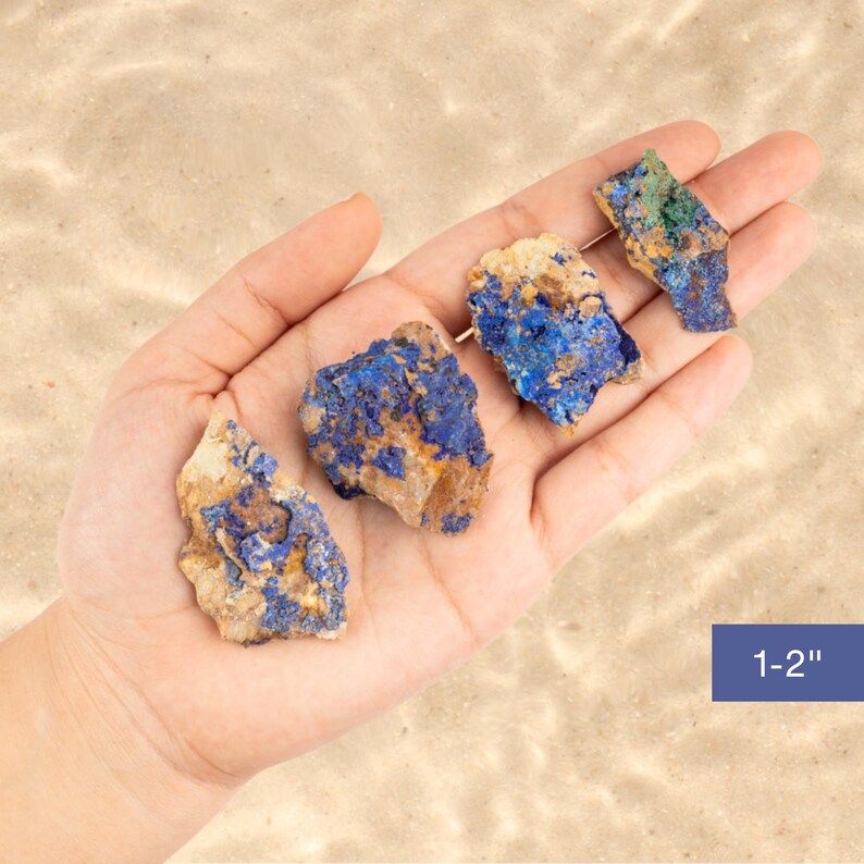 May include: Four rough, natural, blue and brown azurite stones, ranging in size from 1 to 2 inches, are displayed in a hand.