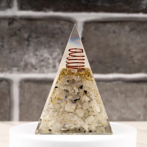 May include: A clear crystal pyramid with a copper wire coil inside. The pyramid is filled with small white crystals and gold glitter.