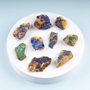 May include: A collection of nine small, rough, natural mineral specimens. The stones are a mix of brown, green, and blue colors. The stones are arranged on a white circular surface.