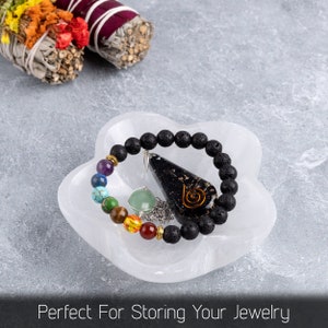 May include: A white selenite charging dish with a black lava rock bracelet, a green aventurine crystal, and a black obsidian pendant with a gold spiral design.