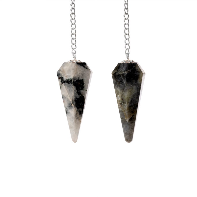 May include: Two gemstone pendulums with silver chains hang against a white background. The pendulums are faceted, with a pointed bottom and a silver cap. One is white and black, the other is gray and black.