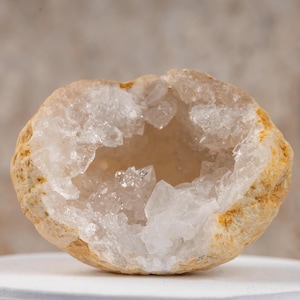 May include: A geode with a white crystal interior and a brown, rough exterior. The geode is sitting on a white surface.
