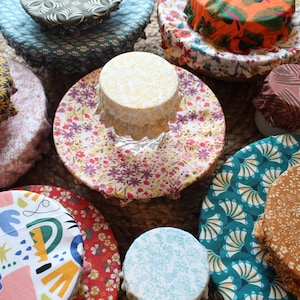 Könnte beinhalten: Eine Auswahl an bunten Stoff-Lebensmittelhüllen mit verschiedenen Mustern, darunter florale, geometrische und abstrakte Designs. Die Hüllen sind aus wiederverwendbarem, waschbarem Stoff gefertigt und eine nachhaltige Alternative zu Plastikfolie.