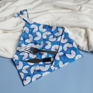 Op de afbeelding: Een blauwe en witte gepatroneerde stoffen servet met een vork en mes erop. Het servet is in een driehoekige vorm gevouwen.