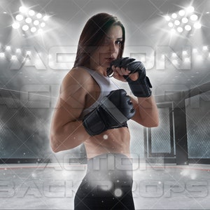 May include: A female athlete wearing black and white boxing gloves stands in a boxing ring. The ring is surrounded by a black metal cage. The background is a blurry image of a stadium with bright lights.