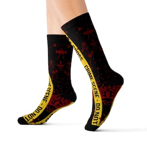 May include: Black socks with a yellow and black crime scene tape design and red blood splatter. The text on the tape reads "Crime Scene - Do Not Cross".