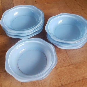 May include: A set of five light blue ceramic bowls with scalloped edges. The bowls are stacked in two piles, with one pile of three bowls and another pile of two bowls.