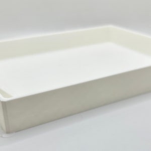 May include: A white rectangular pet litter box with a ramp for easy access. The box has a low profile and is made of a solid, opaque material. The ramp has grooved steps for traction.