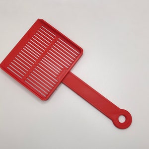May include: A red plastic cat litter scoop with a rectangular slotted head and a long handle. The handle has a circular hole at the end for hanging. The scoop is designed for sifting and cleaning cat litter boxes.