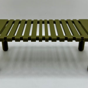 May include: Olive green miniature table with a slatted top and four cylindrical legs. The table is made of plastic and is designed for decorative purposes. The table measures approximately 6 inches long, 3 inches wide, and 2 inches tall.