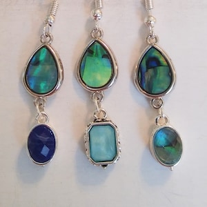 May include: Three pairs of dangle earrings with silver hooks. Each earring has a teardrop-shaped green abalone shell, a smaller teardrop-shaped blue or green abalone shell, and a round or rectangular blue or green gemstone.