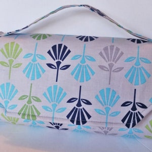 Puede incluir: Una bolsa de tela gris y blanca con un estampado floral azul, verde y gris. La bolsa tiene un solo asa y una cremallera.