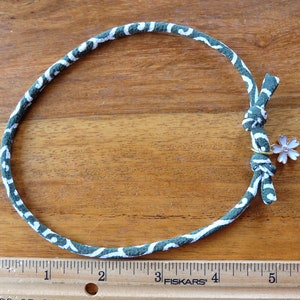 Peut inclure: Un collier en tissu &agrave; motifs verts et blancs avec un petit charme en forme de fleur. Le collier mesure environ 25 cm de diam&egrave;tre. Le charme est une petite fleur rose clair avec un anneau dor&eacute;.