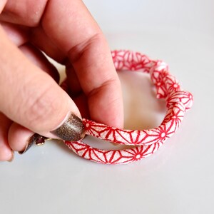 Peut inclure: Un bracelet &agrave; motifs rouges et blancs avec un motif floral. Le bracelet est fait d'une mati&egrave;re douce semblable &agrave; du tissu et est tenu par une main. Le bracelet est de forme circulaire.