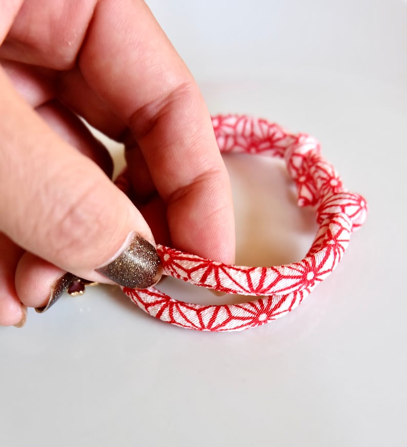 Peut inclure: Un bracelet &agrave; motifs rouges et blancs avec un motif floral. Le bracelet est fait d'une mati&egrave;re douce semblable &agrave; du tissu et est tenu par une main. Le bracelet est de forme circulaire.