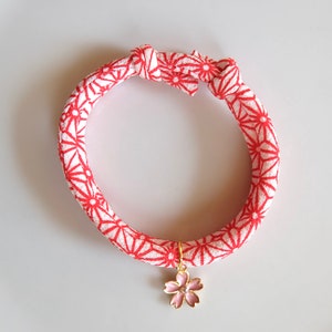 Peut inclure: Un collier pour animaux de compagnie &agrave; motif rouge et blanc, orn&eacute; d'un charm en forme de fleur de cerisier dor&eacute;. Le collier est nou&eacute; en haut.