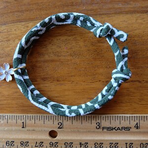 Peut inclure: Un bracelet en tissu &agrave; motifs verts et blancs avec un charm en forme de fleur blanche. Le bracelet est nou&eacute; aux extr&eacute;mit&eacute;s et poss&egrave;de un anneau dor&eacute; retenant le charm. Le bracelet mesure environ 12,7 cm de long.