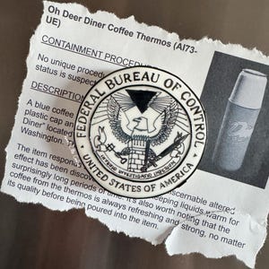 May include: A black and white Federal Bureau of Control emblem, with the words "Federal Bureau of Control" and "United States of America" encircling an eagle. The emblem is on a white background. A blue and white coffee thermos is also visible.